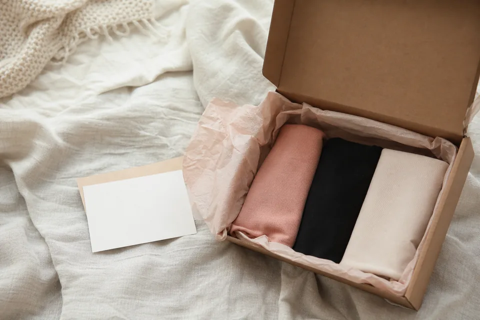 Opened mailer box with tissue paper and three folded pairs on a bed